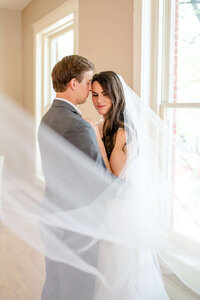 Married couple snuggled up with her veil draped around.