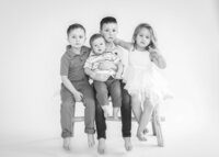 Four small siblings on a bench in a studio session captured by McKinney  studio photographer Allison Amores