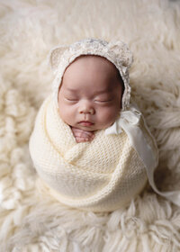 Newborn baby girl wrapped in a soft hand-knitted cream wrap during her studio session at Jennifer Brandes Photography in South Central Minnesota.