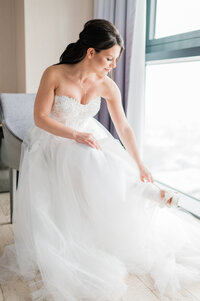 Bride sits while putting on her wedding heels