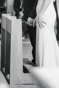 Black and white close up image of a bride and groom standing in front of a kneeling bench