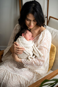 Mother holding her new baby while wearing a white dress