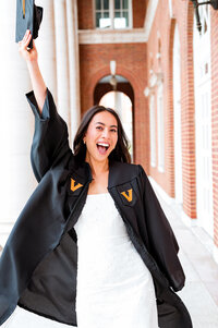 Senior wearing white dress and Vanderbilt robe smiling with cap in the air