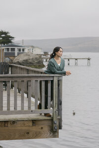 Model in a soft green wrap cardigan leaning on a weathered boardwalk railing