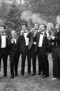 Black and White image of groom and groomsmen smoking cigars in tented wedding