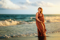 Expectant mother standing in the surf during a sunset maternity session on the North Carolina coast