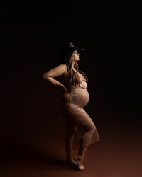 Pregnant woman wearing a sheer rhinestone maternity gown and cowboy hat during a dramatic studio maternity photography session by Kaitlyn Dawn Photography.