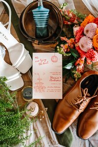 Wedding invitation, shoes, rings, florals and accessories styled in a colorful New England wedding flatlay.