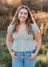 teenage girl standing in a field with her hands in her pockets smiling and wearing  jeans