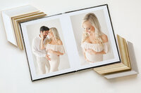 Open heirloom album displaying studio maternity portraits in soft neutral tones