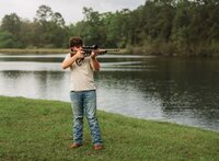 Senior portrait at Circle B Lake in Wilmer, Alabama — aiming an unloaded hunting rifle off into
the distance, looking through the scope.