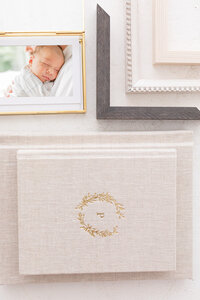 Photo of a sleeping baby in a matted frame, placed on white table in front of white wall, next to a white vase containing dried wheat
