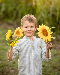 Young boy smiling with dirt on his hands from picking sunflowers during a child portrait session in a sunflower field in Callahan. - A portrait experience by Nature's Child Photography.