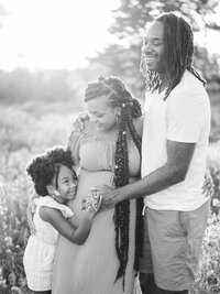 Black and white image of a family laughing and touching mom's pregnant belly