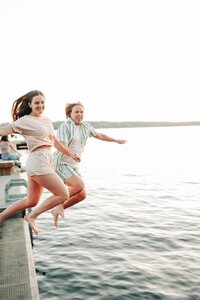 A couple, jumping into the water off of a dock.