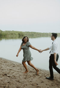 Celisia and Andrew running along a lake on the beach holding hands