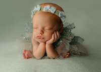 Sleeping newborn baby girl wearing a delicate floral headband and posed on a soft green backdrop during a studio session with newborn photographer Kaitlyn Dawn Photography.