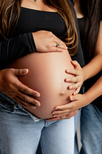 Close-up of a pregnant woman’s belly with family hands gently resting on it, capturing a heartfelt pregnancy moment during an Inland Empire session by Kaitlyn Dawn Photography.