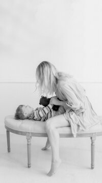 An in studio mommy and me photo of a mother on a bench with her baby boy playing.