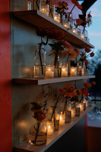 Romantic candlelit floral display at Callie and Hayes’ Burritt on the Mountain wedding reception, featuring glass bottles with flowers and glowing votive candles arranged on wooden shelves.