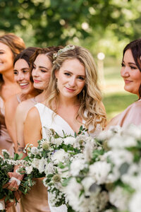 Wedding party photo—bride with bridesmaids holding bouquets outdoors in soft summer light