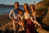 Family of four posing at sunset on baker beach with the golden gate bridge in the background