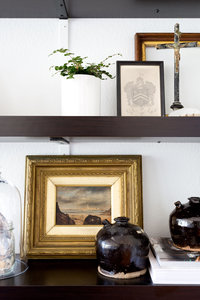 Dark brown bookshelves with gold framed oil painting, and vintage pottery