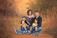 Family of four sitting in warm fall field during autumn portrait session in Eastern North Carolina