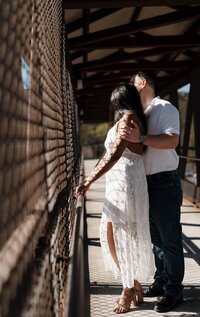 Engaged couple standing on the pedestrian bridge overlooking the train tracks in Marietta Square, sharing a quiet moment in the sunlight during their engagement photo session