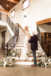 Bride standing on stairs looking down at groom holding her hand