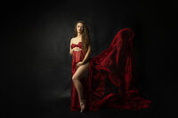 Expectant mother poses during her fine art luxury maternity session with a red silk scarf.