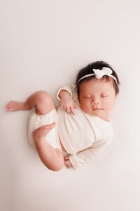 Studio newborn portrait in Elk Grove with warm beige and ivory tones, showcasing a curled sleeping baby in a classic posed style