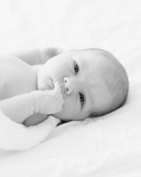 Black and white portrait of an awake newborn baby resting on a bed during an in-home lifestyle newborn session.