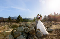 Bride and groom sharing a kiss on large mountain rocks during a wedding photography session in Graeagle, California with Nature’s Child Photography, surrounded by pine trees, open sky, and warm sunset light across the Sierra landscape.