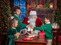 Children sharing cookies and milk with Santa during a Santa's Magical Christmas photography session in Jacksonville, Florida with Nature's Child Photography, gathered around a festive holiday table filled with Christmas treats, North Pole details, and cozy fireplace magic.