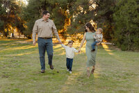 Parents walking hand in hand with their young son through a grassy park at sunset, relaxed lifestyle family portrait by Kaitlyn Dawn Photography.