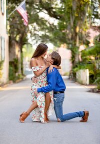 Professional photography by Nature's Child Photography: St. Augustine engagement capturing a joyful proposal moment, the groom-to-be kneeling on the street while she cups his face and leans in close.