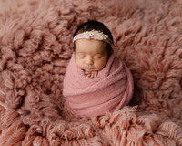 Sleeping newborn baby girl wrapped in a blush pink swaddle and posed on a fluffy pink blanket during a professional newborn photography session by Kaitlyn Dawn Photography.