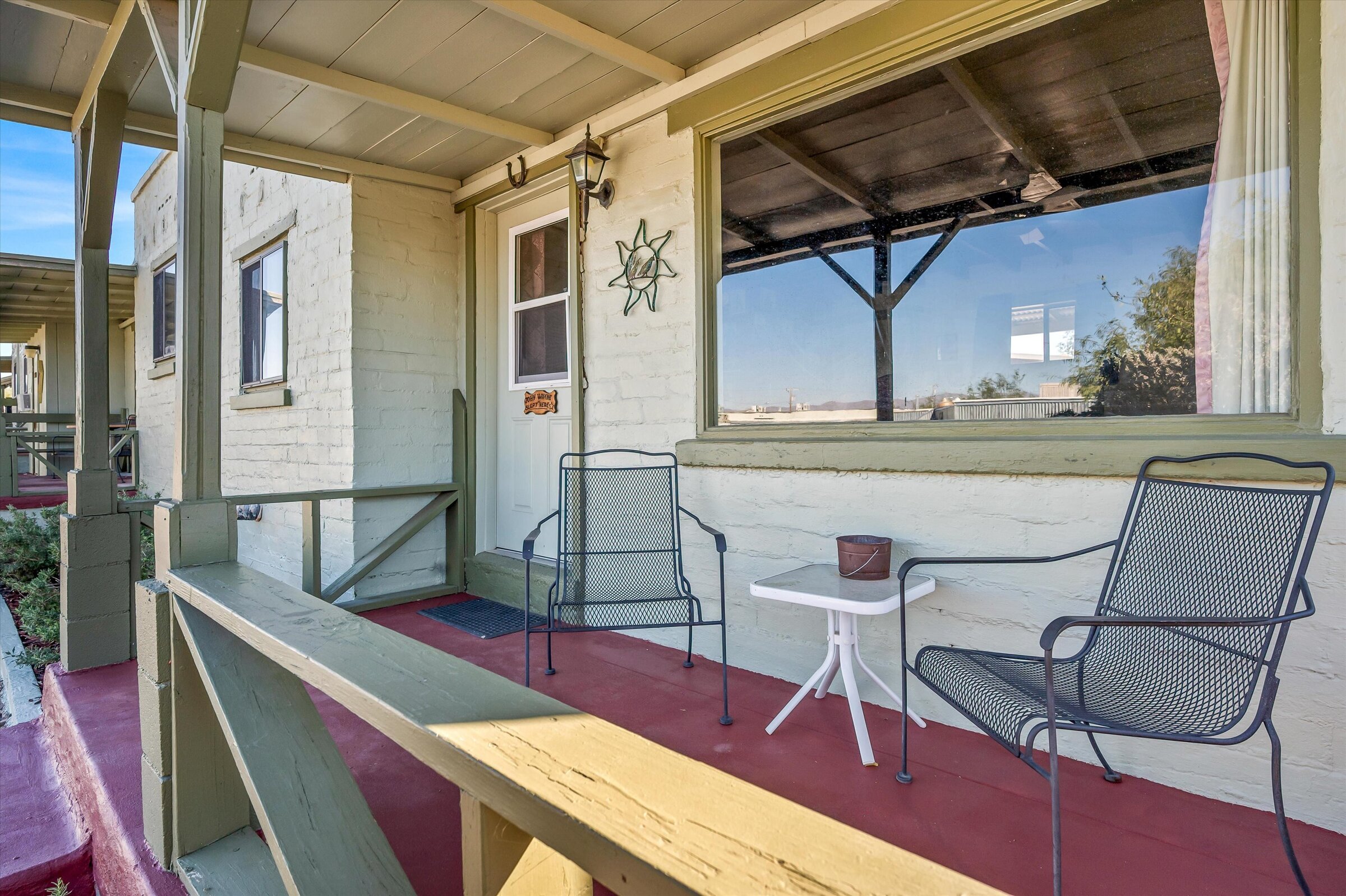 A small porch with two metal chairs and a small table in front of a white brick building.