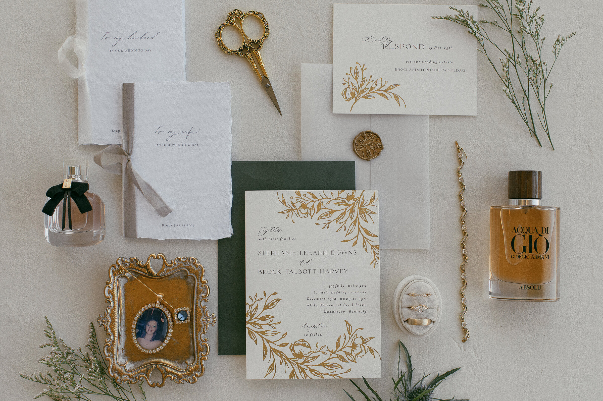 Wedding flat lay with invitation suite, perfume, jewelry, and handwritten letters.