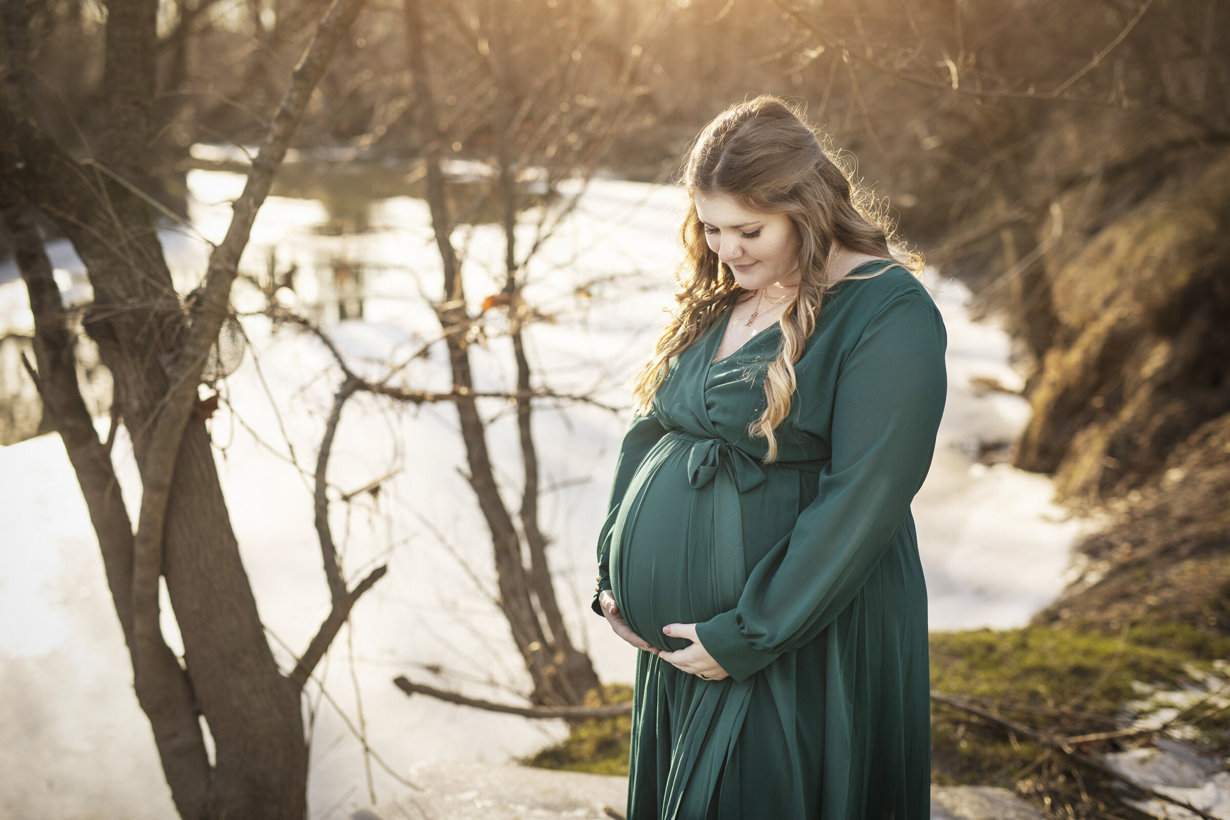 Pregnant mother in greewn gown standing in front of a frozen river in beautiful light in Bucyrus Ohio