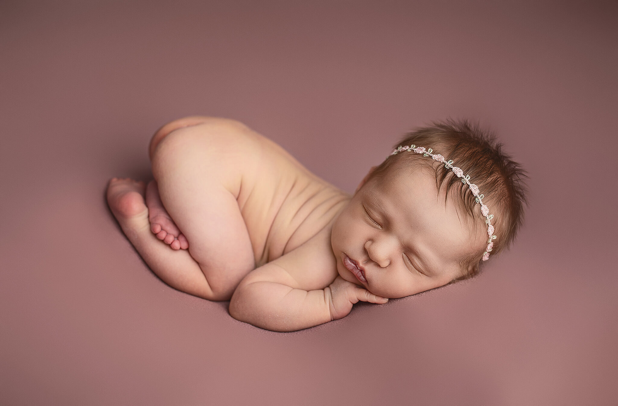 Newborn baby girl on pink blanket all snuggled up and sleeping