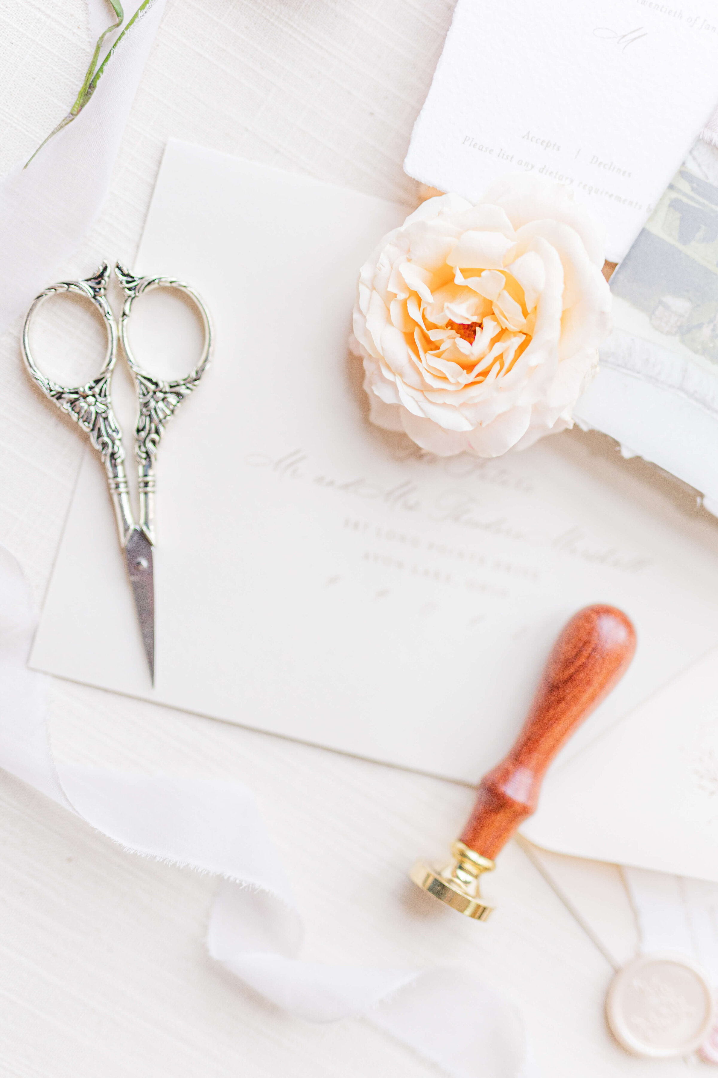 A wedding detail flat lay of a peachy flower, scissors, a stamp and envelopes