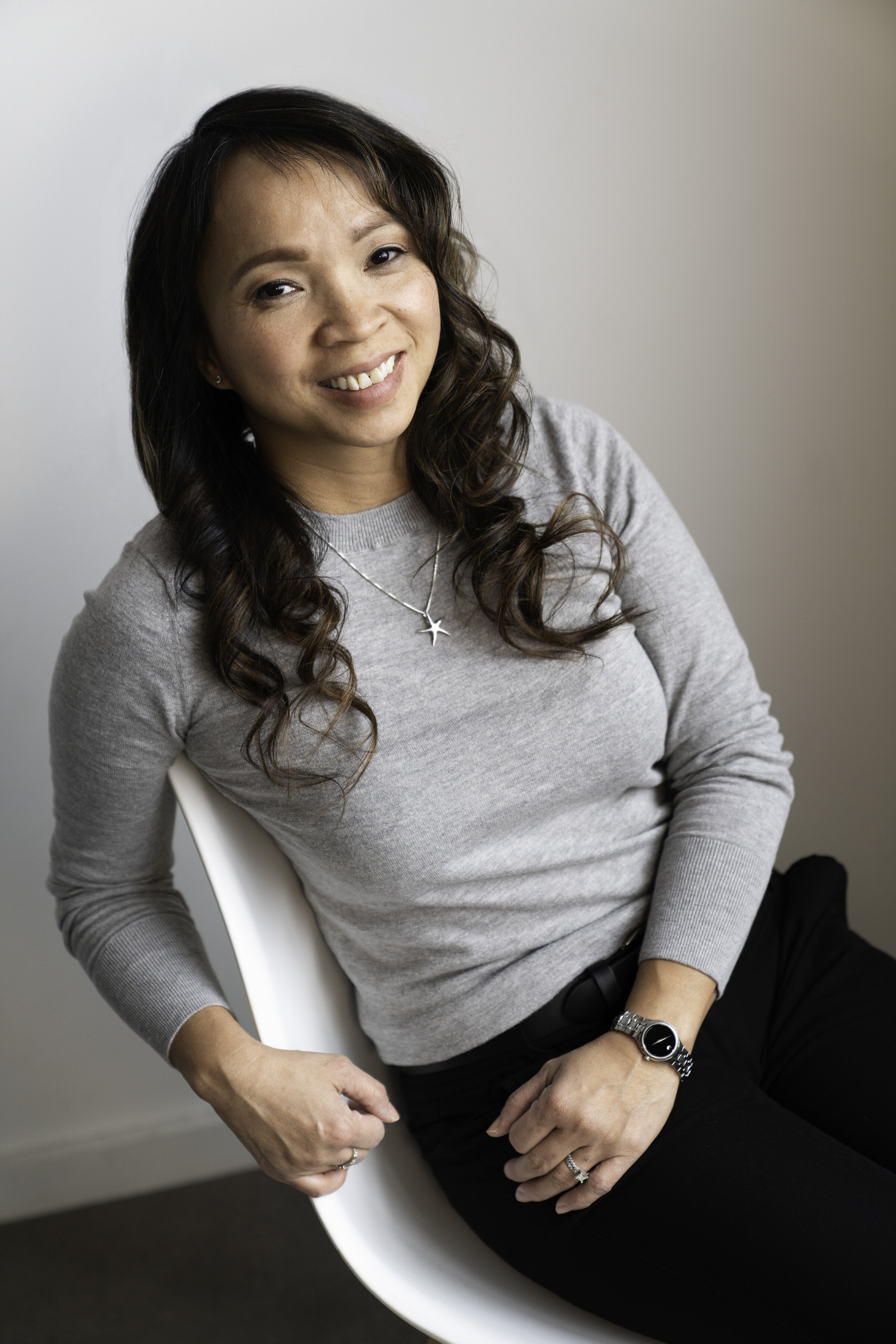 Woman sitting in a chair and smiling at the camera for her professional headshot