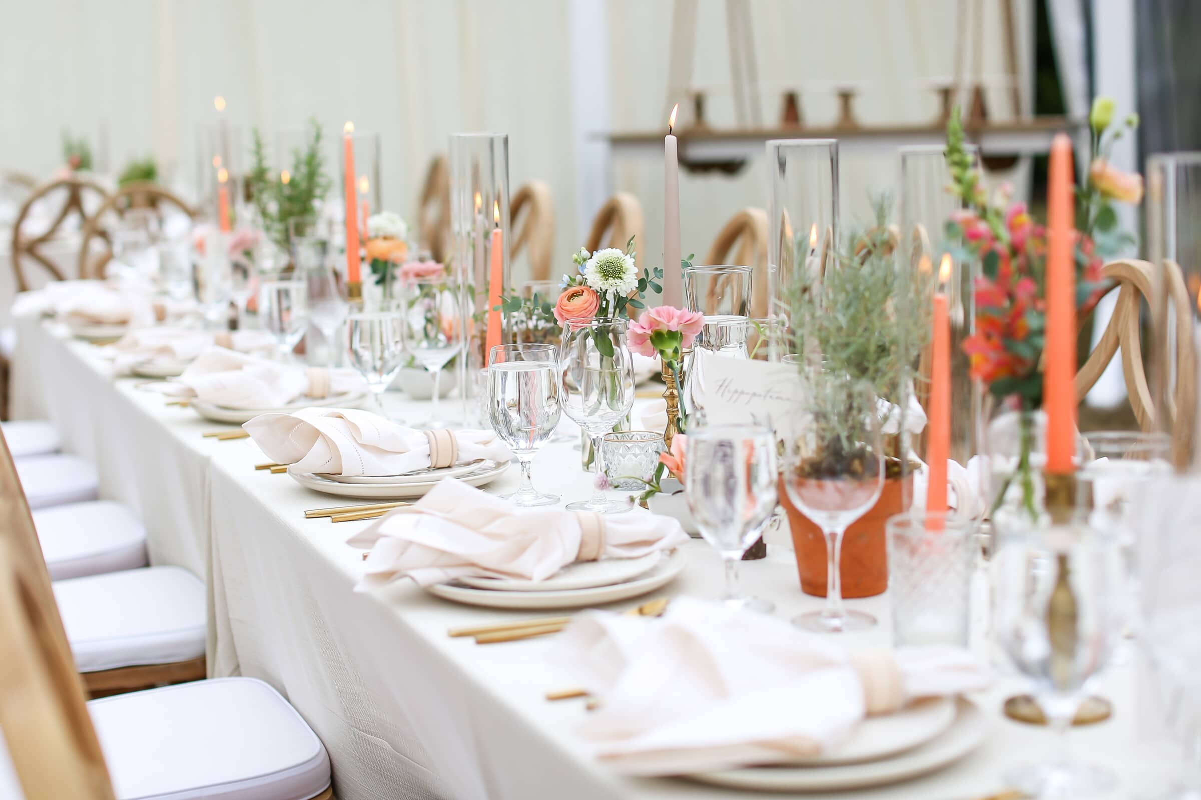 long table decorated with neutral place settings and orange candles and greenery  at a wedding reception in Chapel Hill