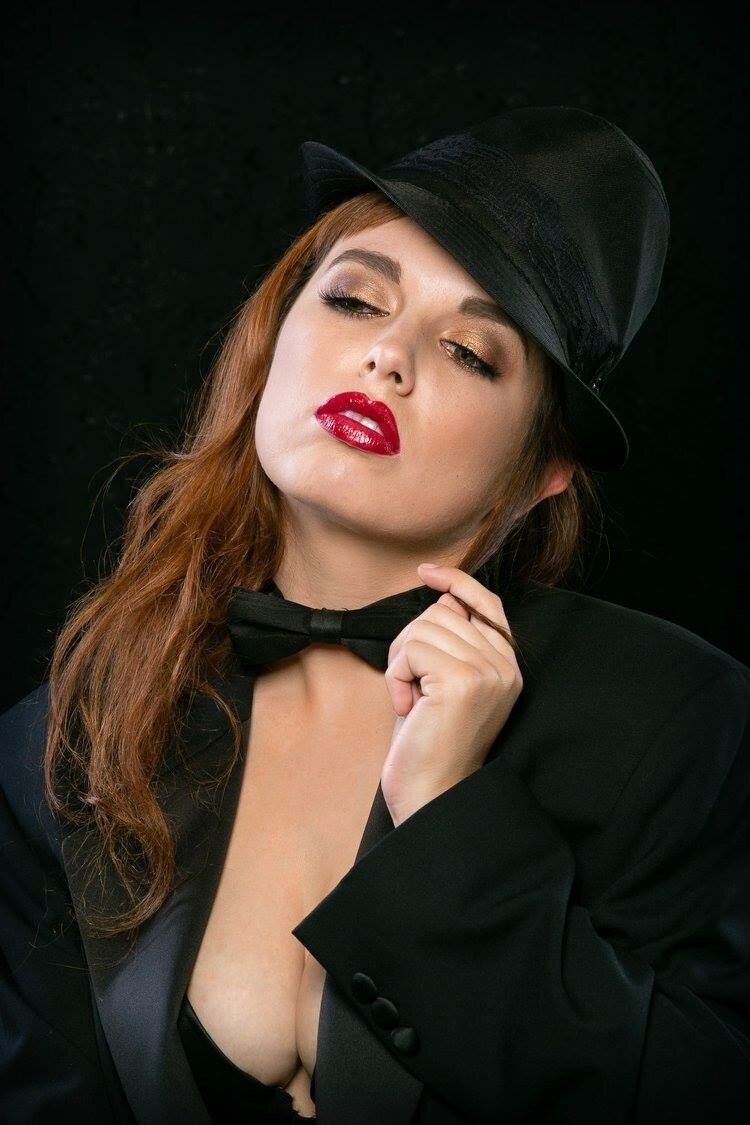 A woman in an open blouse with red lipstick  and a black fedora.