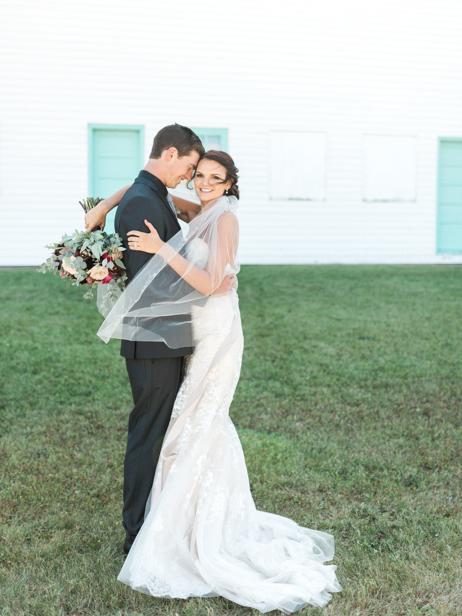 Groom and bride embrace while holding florals