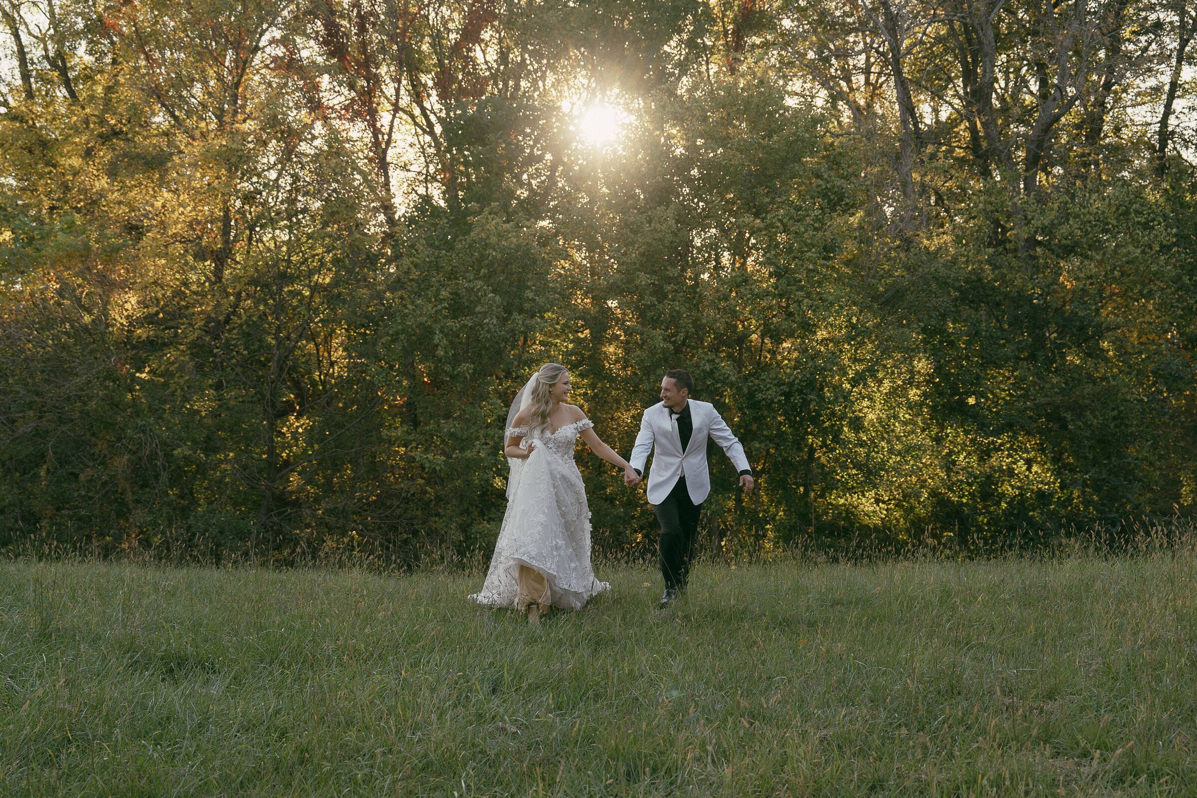 Bride and groom walking through a sunlit field.