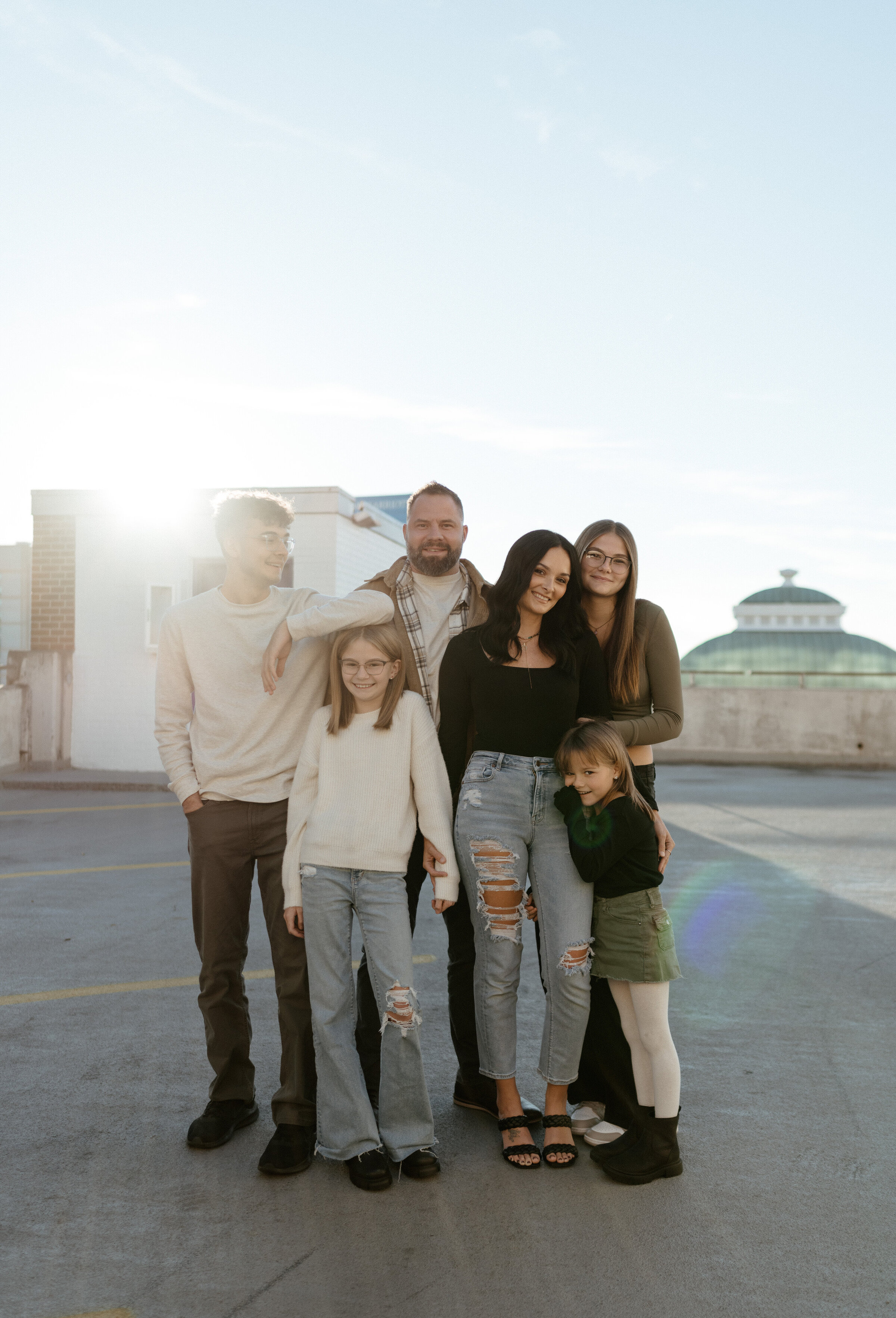 A family of six stands huggiing at sunset on a parknig garage roof in downtown Indianapolis