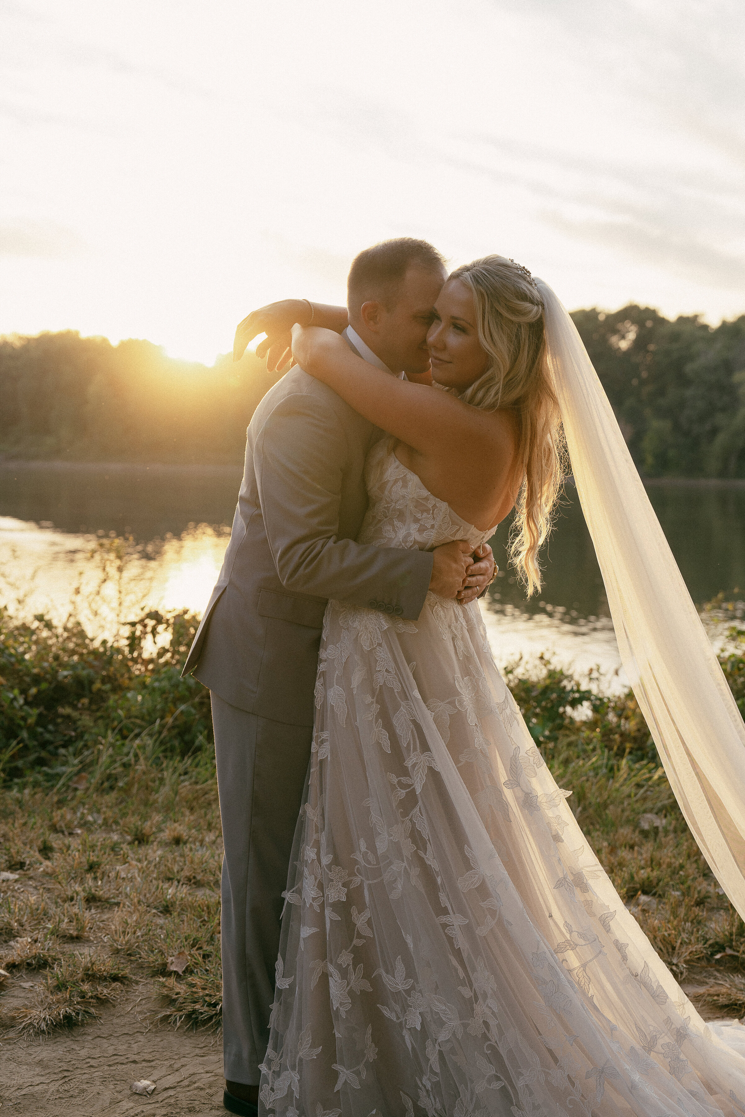 Bride and groom embracing at sunset by the river.